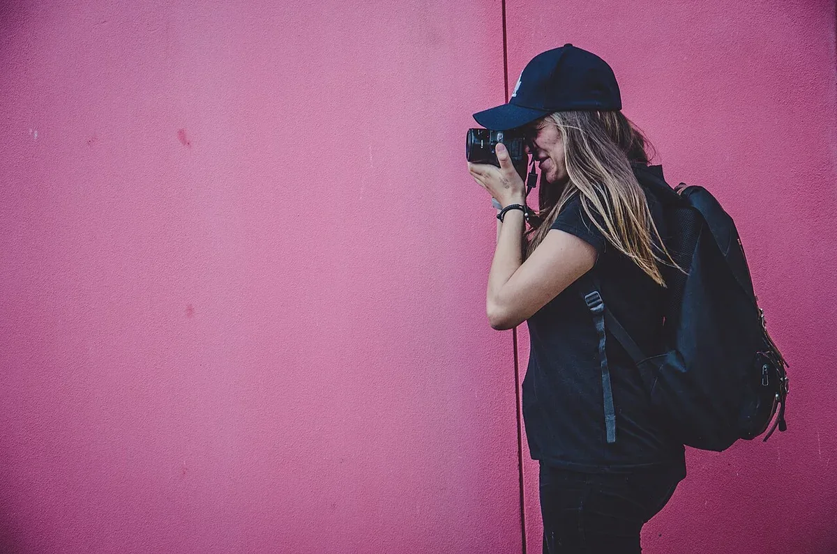 A photographer using a camera beside a pink wall