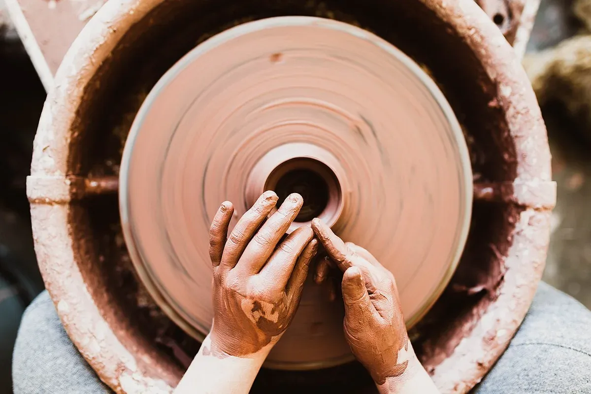 Hands shaping clay on a spinning pottery wheel