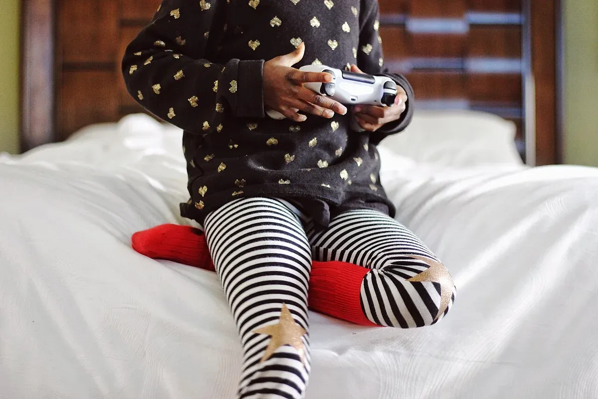 A young player holding a game controller while sitting on a bed