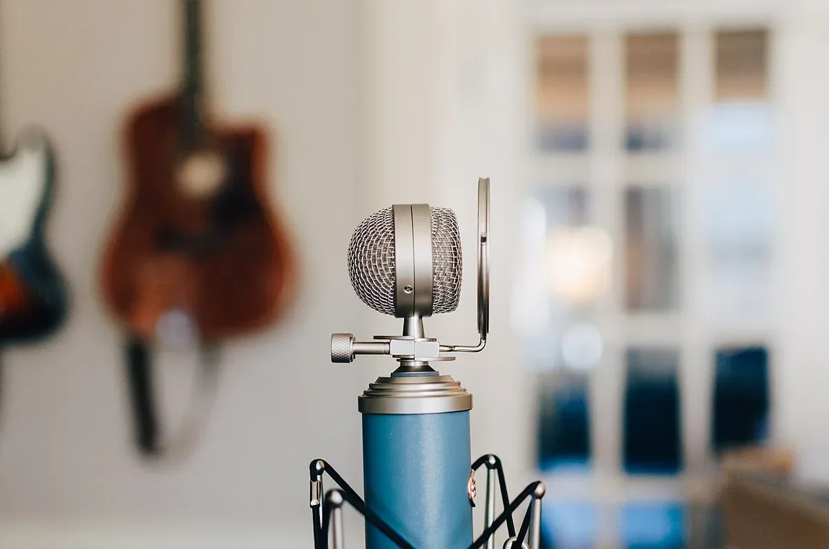 A studio microphone with guitars softly visible behind it