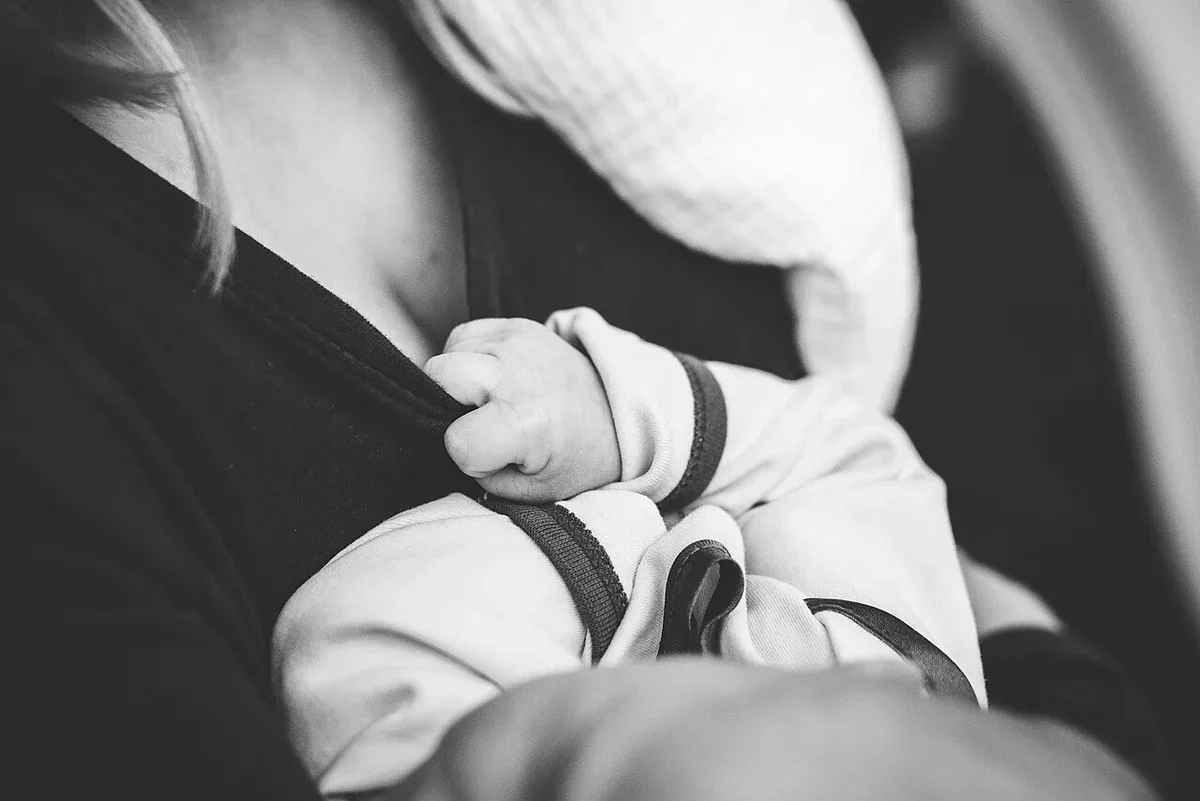 A small baby's hand holding an adult's clothing