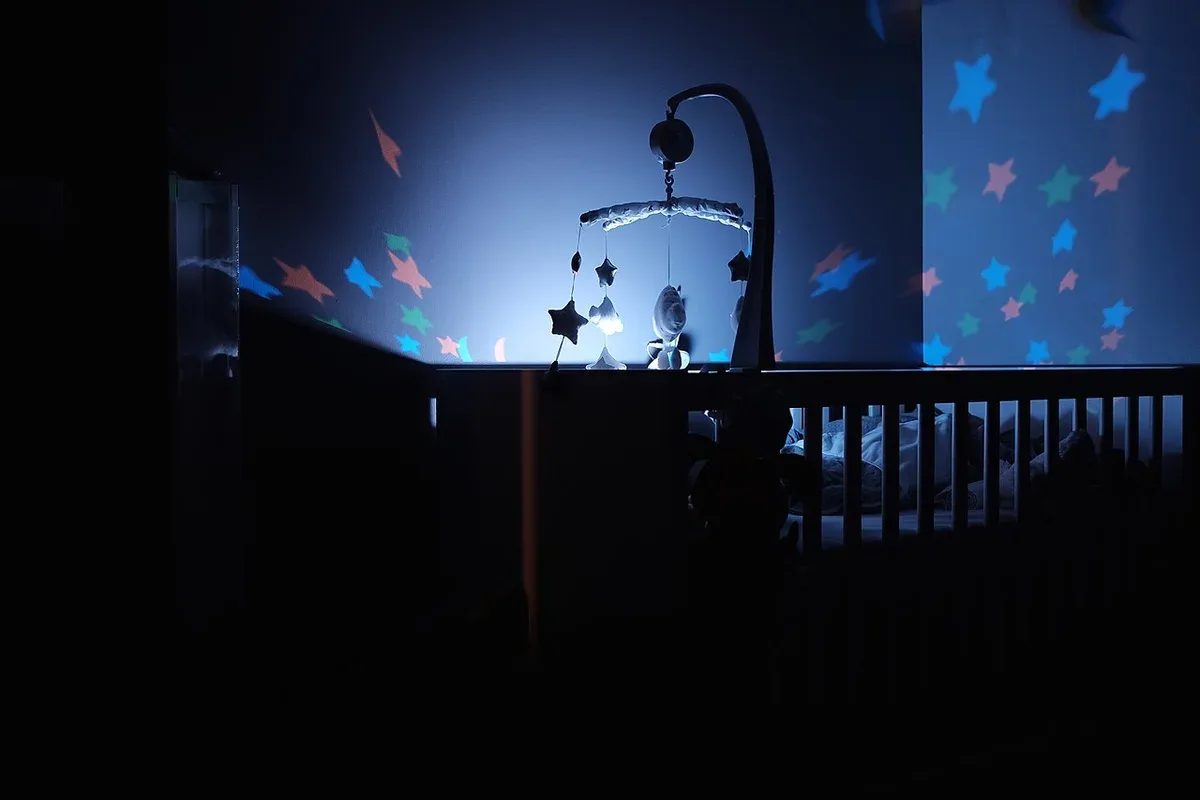 A crib and hanging mobile in a dim room with star-shaped lights