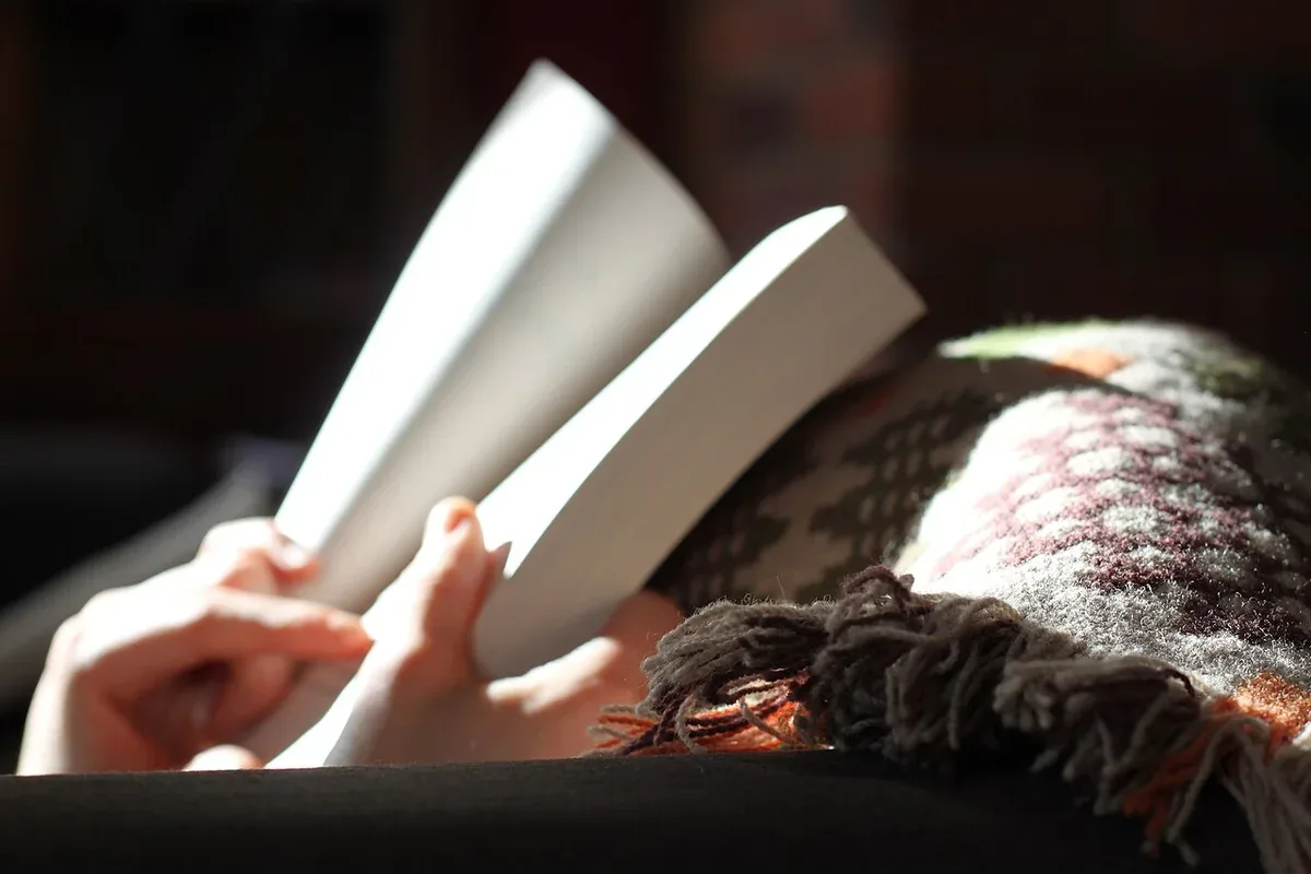 A person reading a book beneath a textured blanket