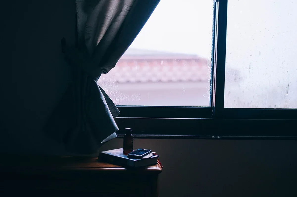 A book on a small table beside a curtained window